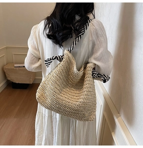 Detail of woven straw tote bag with black and white striped rope shoulder strap