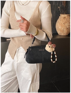 Detail of black leather handbag featuring plush bear charm and beaded decorative chain