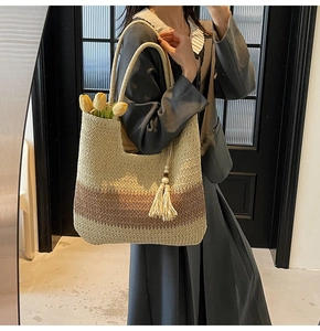 Macro view of woven straw tote bag featuring contrast stitching and decorative tassel
