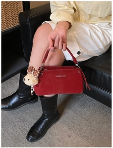 Detail of red crossbody bag with plush bear charm and metallic brand logo plaque