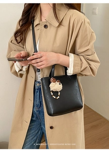 Détail du sac seau noir en cuir avec charm d'ours mignon et accessoires en perles