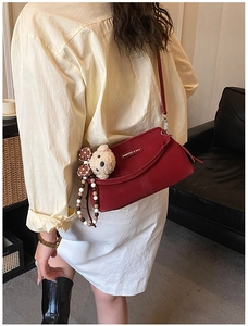 Close-up of a deep red leather crossbody bag featuring a plush bear charm and beaded chain