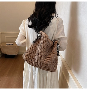 Detail of woven straw shoulder bag featuring a chic black and white striped silk scarf strap