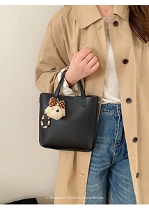 Détail du sac cabas en similicuir noir avec breloque ours sur un trench-coat kaki