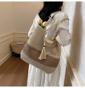 Detail of woven straw tote bag with gradient color texture and bohemian tassel charm