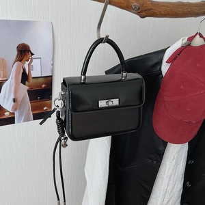 Detail einer schwarzen glänzenden quadratischen Handtasche mit Fransen-Quastenanhänger