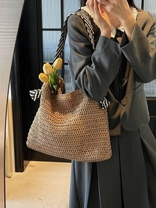 Handwoven straw tote bag with black and white striped straps and bow accent for beach