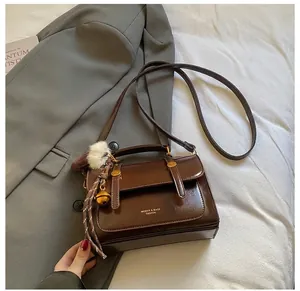 Details einer braunen Vintage-Lederhandtasche mit Seidenschal und weißem Pompon
