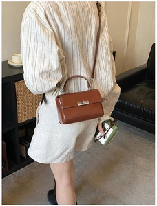 Detail of a brown patent leather crossbody bag with silver twist lock on a model