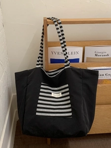 Black canvas tote bag with striped shoulder straps and large front pocket in a minimalist room