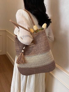 Three-tone woven straw tote bag in brown and cream with a tassel charm on a model