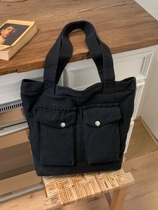 Vielseitige schwarze Canvas-Einkaufstasche mit Vordertaschen und Schnallen auf Holztisch