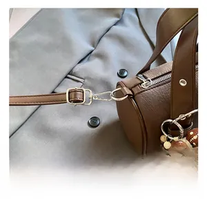 Detail of adjustable strap and metal swivel hook on brown litchi leather barrel bag