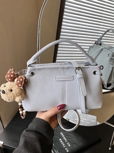 Light blue crossbody bag with top handle and cute bear pendant shown in a hand