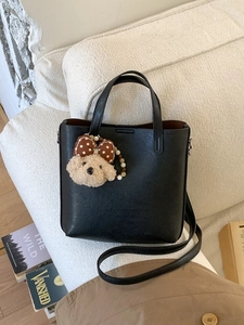 Sac fourre-tout classique en cuir PU noir avec charm chien en peluche sur un canapé blanc