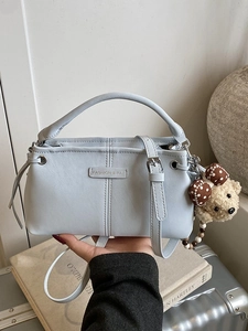 Blue faux leather crossbody bag with top handle and cute bear charm in lifestyle setting