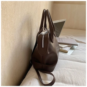 Detail view of smooth coffee brown leather texture and silver zipper on shell bag