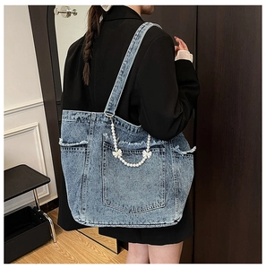 Detail of blue denim tote bag featuring frayed edges, pearl chain, and white bow accent
