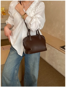 Detail of a dark brown leather shell bag with top handles and matte finish in a lifestyle setting