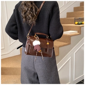 Details der glänzenden braunen Retro-Handtasche mit süßem Handschuh-Anhänger und Pompon