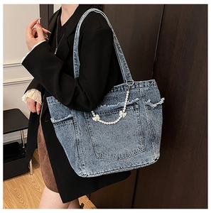 Detail of denim tote bag with pearl bow chain and frayed edges in light blue wash
