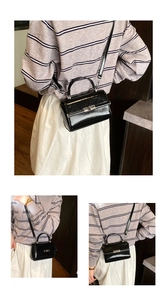 Close-up of a glossy black square crossbody bag with vintage buckle and top handle