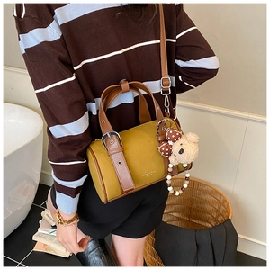 Detail of retro cylinder bag in mustard and caramel leather with a cute teddy bear charm