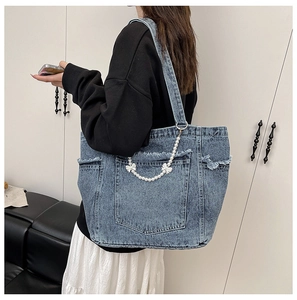 Detail of light blue washed denim tote bag featuring pearl chain and bow accessory