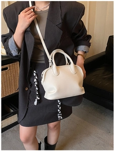 Detailed view of beige shell bag with lychee texture and silver zipper on model