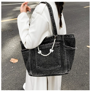Detail of grey denim tote bag with frayed edges, pearl chain and bow accents