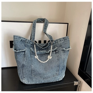 Macro detail of retro denim tote bag with frayed pockets and white bow pearl charms