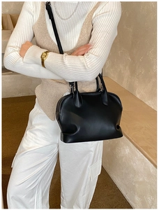 Black leather shell bag shown at a 45-degree angle worn by a model in casual style