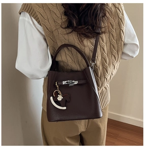 Detail of dark brown lychee leather bucket bag featuring silver buckle and horse charm