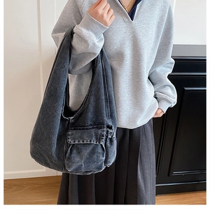 Detail of grey washed denim hobo bag featuring utility flap pocket and white stitching