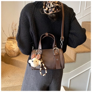 Deep brown litchi pattern Boston bag with teddy bear charm shown on a shoulder