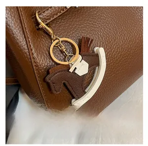 Detail of a brown and white horse-shaped leather charm with a gold metal spring clasp