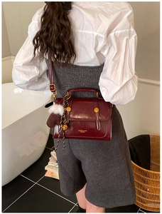 Detail der weinroten Leder-Mini-Viereckstasche mit Goldteilen und Plüsch-Anhänger am Gurt