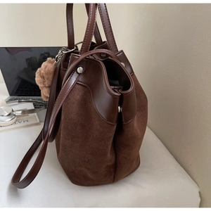 Détail du sac cabas en daim marron foncé avec rivets métalliques et pompon dans un bureau