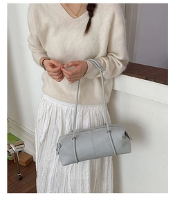 Close-up of minimalist light blue barrel shoulder bag with dual straps on a table