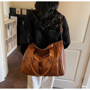 Detail view of brown crocodile embossed tote bag featuring two front zipper pockets