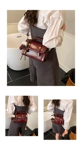 Detail einer weinroten Lederhandtasche mit Goldverschluss und Plüschglockenanhänger