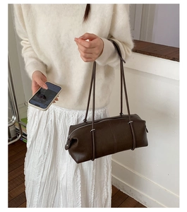 Dark brown leather cylindrical underarm tote bag shown on a model in a minimal setting