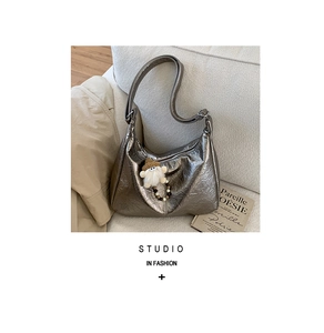 Detail of silver pleated hobo bag with plush charm on white sofa in lifestyle setting