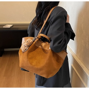 Détail du sac cabas en daim carmél avec pendentif ours porté sur un blazer noir