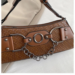 Detail of woven leather texture on a brown shoulder bag with chain and rivet accents
