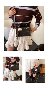 Details einer glänzenden schwarzen Lackledertasche mit Pompon-Anhänger und Trageriemen