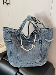 Blue denim tote bag with frayed edges pearl chain and bow accents in a minimalist setting