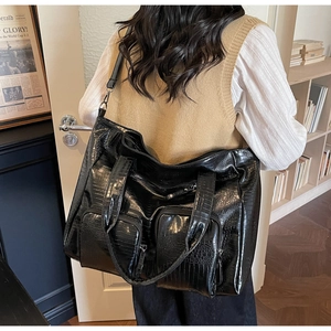 Detailed view of black crocodile pattern tote bag with front zippers on a model