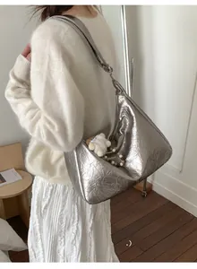 Detail view of silver tote bag with crinkled texture, wide strap and plush pendant