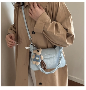 Detail of light blue square bag with woven handle and plush bear charm on a trench coat